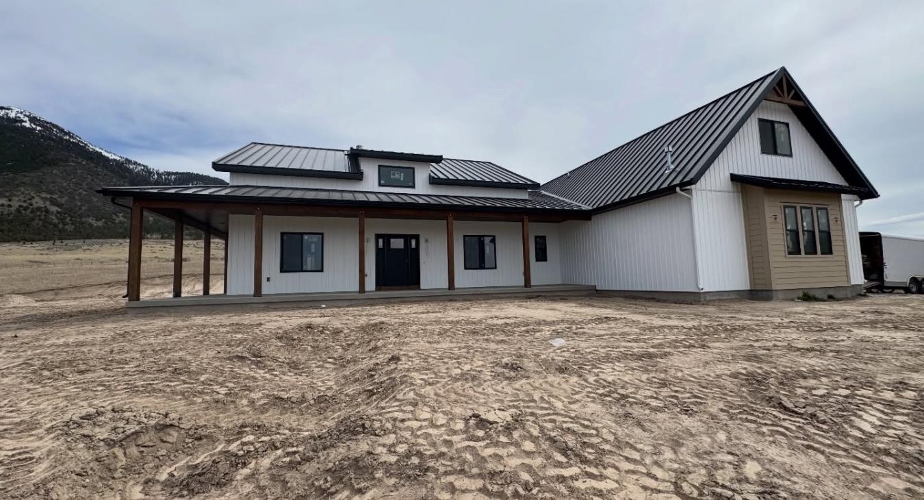 Completed Finn Construction custom modern farmhouse with metal roof covered porch and mountain backdrop in Eastern Idaho
