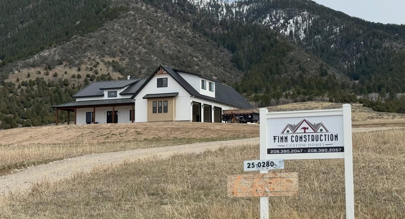 Finn Construction Custom Homes job sign in front of completed modern farmhouse with snow capped mountains Eastern Idaho