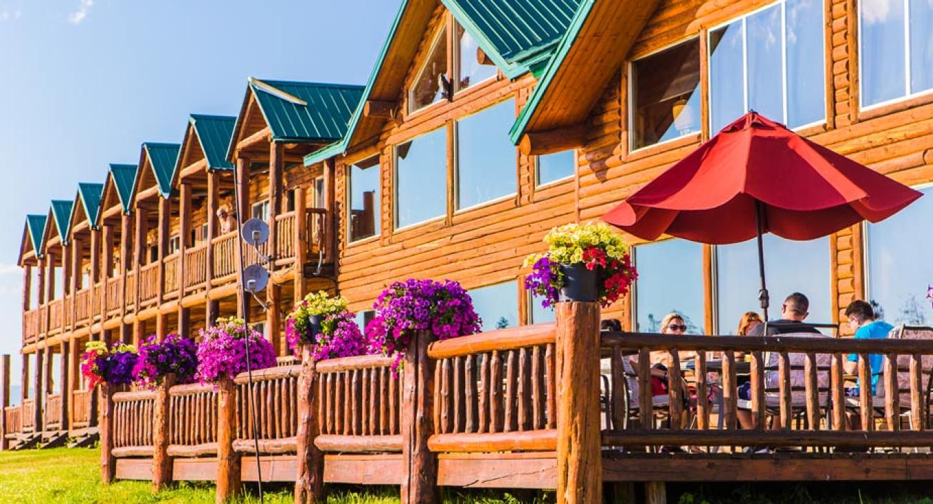 Exterior of Anglers Lodge showing log cabin rooms with flower boxes and outdoor dining deck in Island Park Idaho