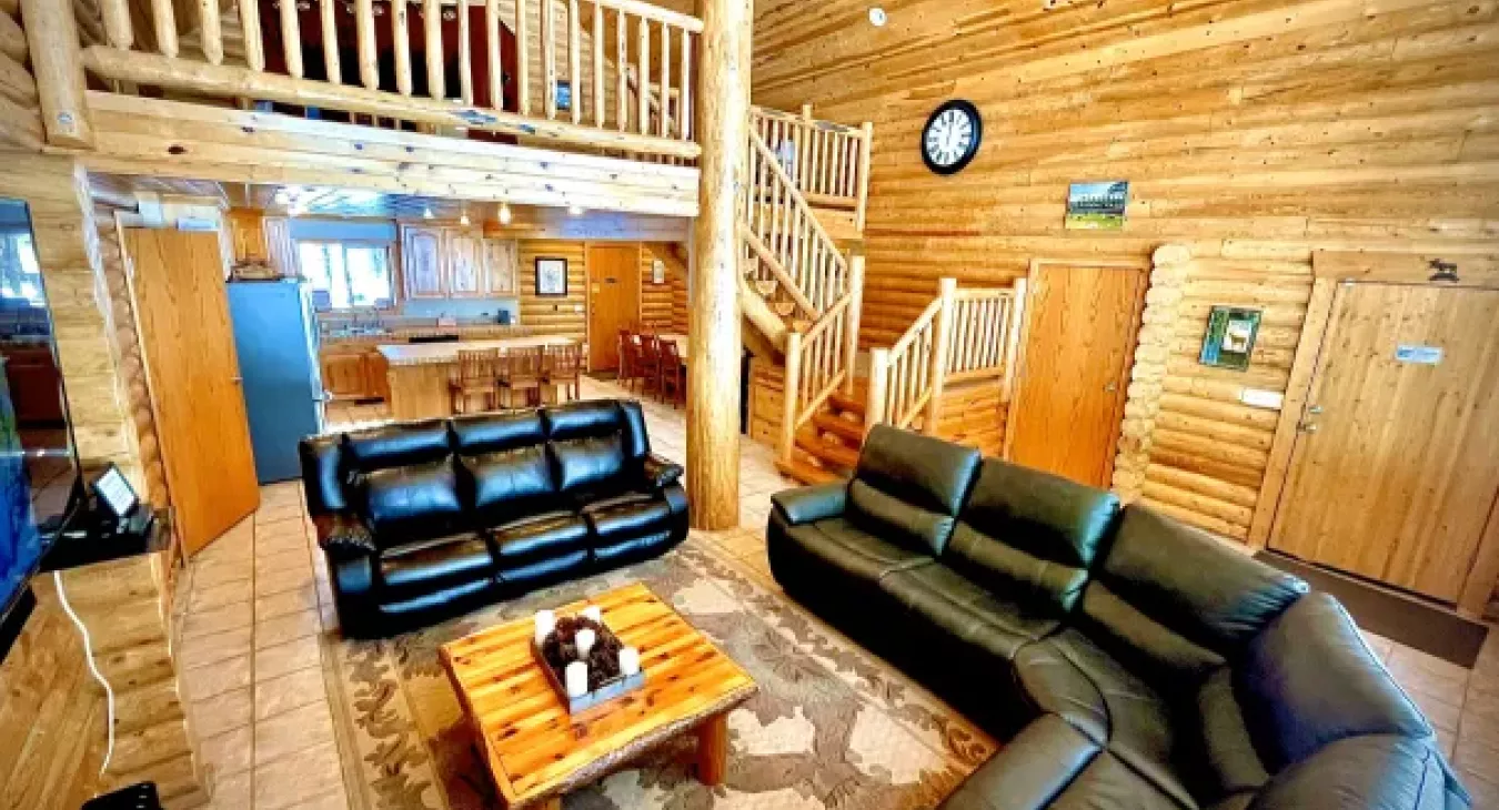 Open concept log cabin living room with two-story windows and loft overlooking nature in Island Park Idaho