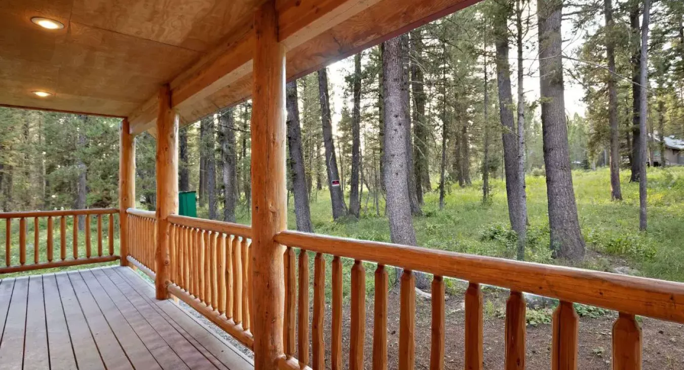Covered front porch with log railing overlooking lodgepole pine forest at Island Park Idaho cabin rental