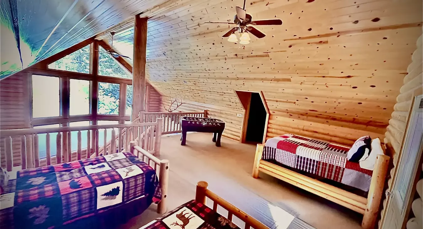 Open loft sleeping area with three log frame beds foosball table and balcony views at Island Park cabin