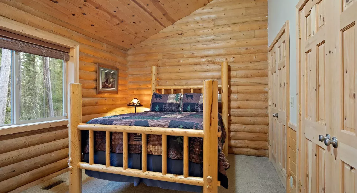 Master bedroom with log frame queen bed and forest views at Yellowstone Log Cabin Island Park Idaho