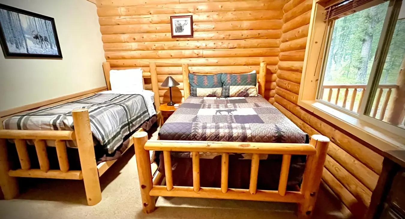 Guest bedroom with log frame double and twin beds and wildlife decor at Island Park Idaho cabin rental