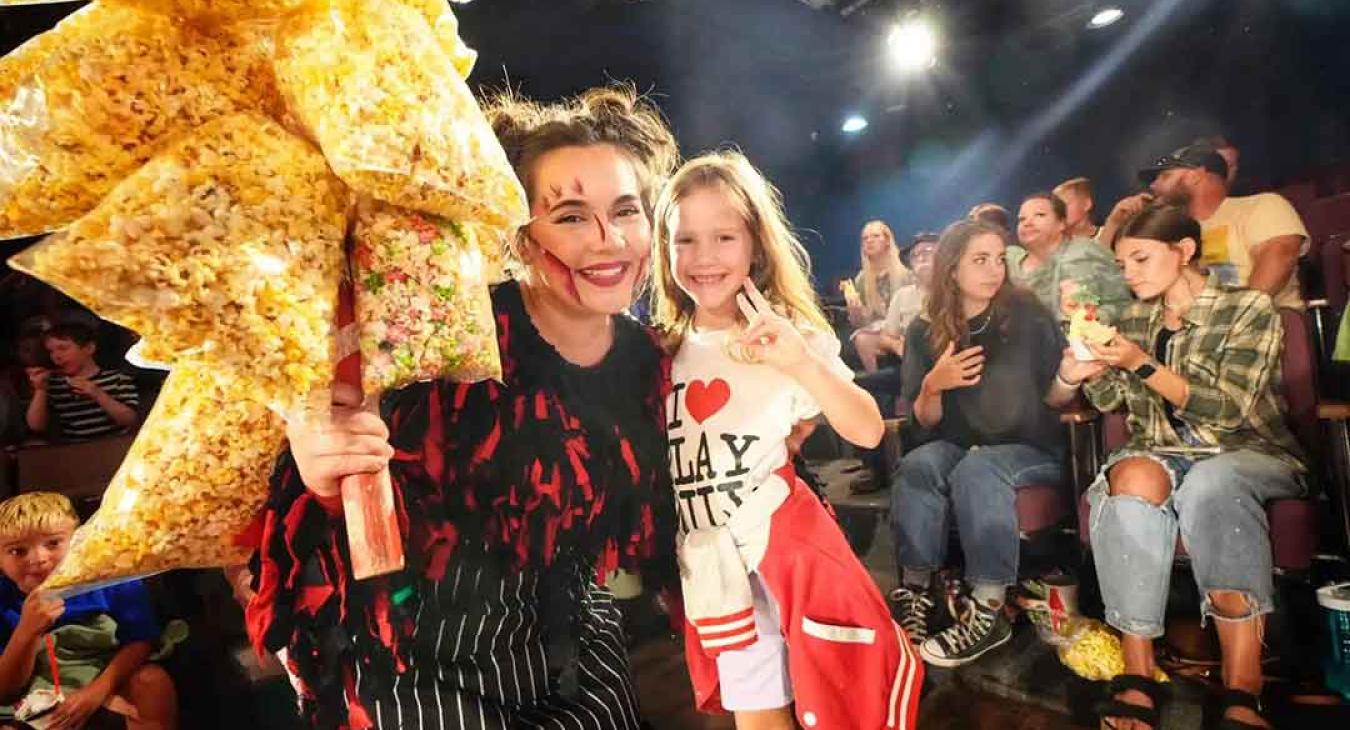 Playmill Theatre cast member selling specialty popcorn to young fan wearing I Love Playmill shirt during intermission at Island Park Idaho