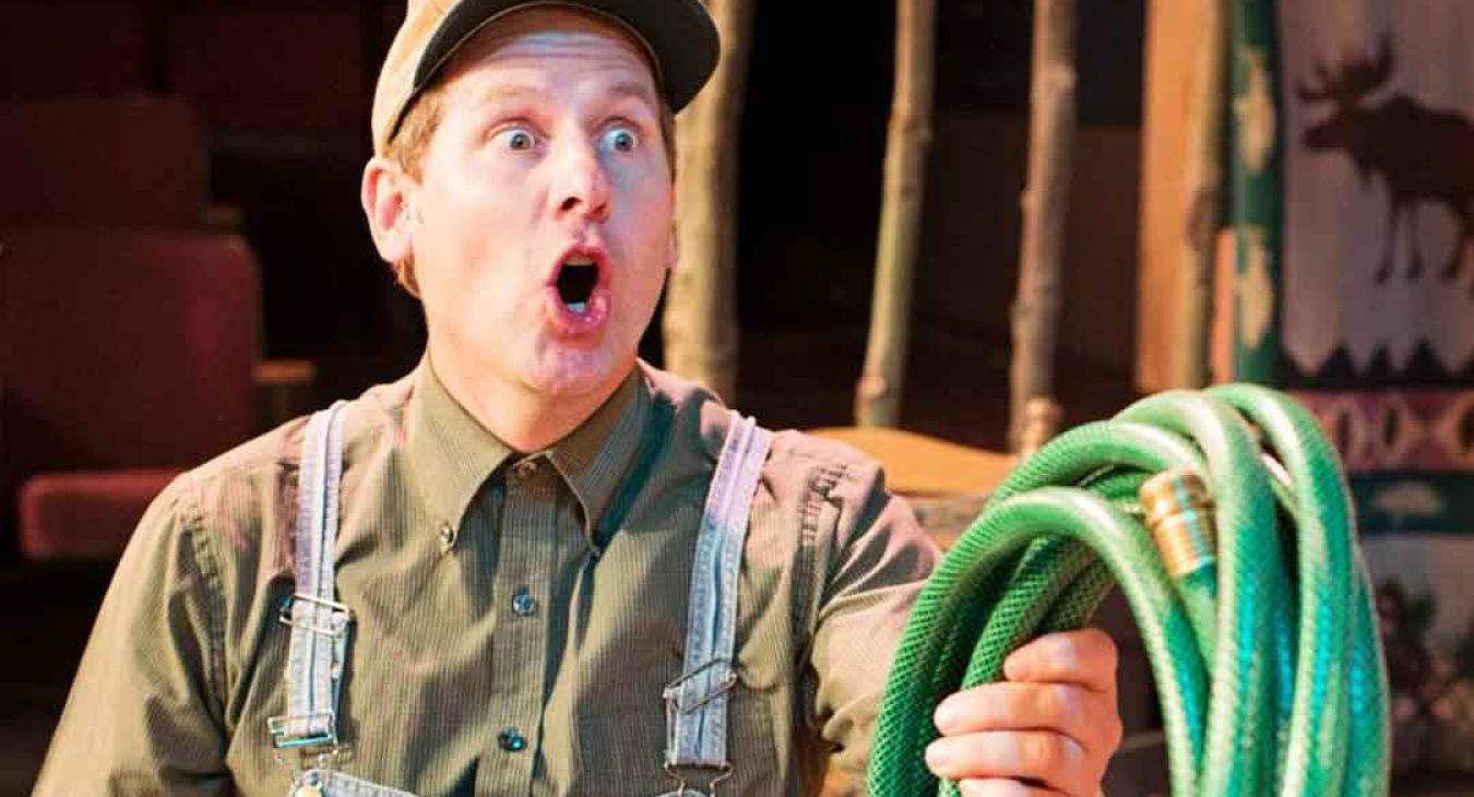 Playmill Theatre actor in comedy role with overalls and garden hose on stage near Yellowstone