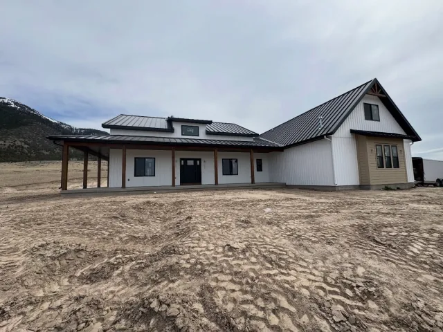Completed Finn Construction custom modern farmhouse with metal roof covered porch and mountain backdrop in Eastern Idaho