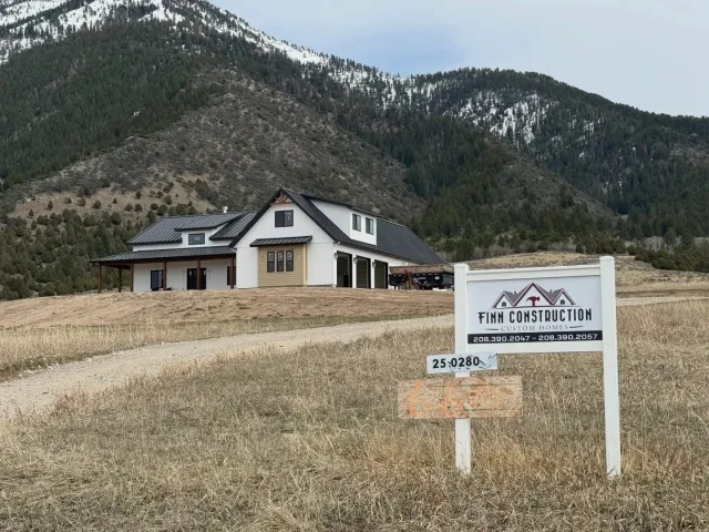 Finn Construction Custom Homes job sign in front of completed modern farmhouse with snow capped mountains Eastern Idaho