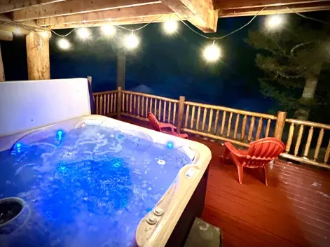 Private outdoor hot tub with string lights and mountain views at Yellowstone Log Cabin Island Park