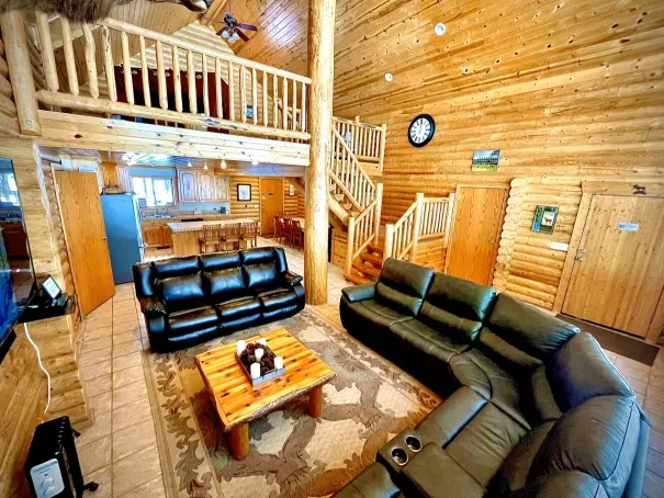 Open concept log cabin living room with two-story windows and loft overlooking nature in Island Park Idaho